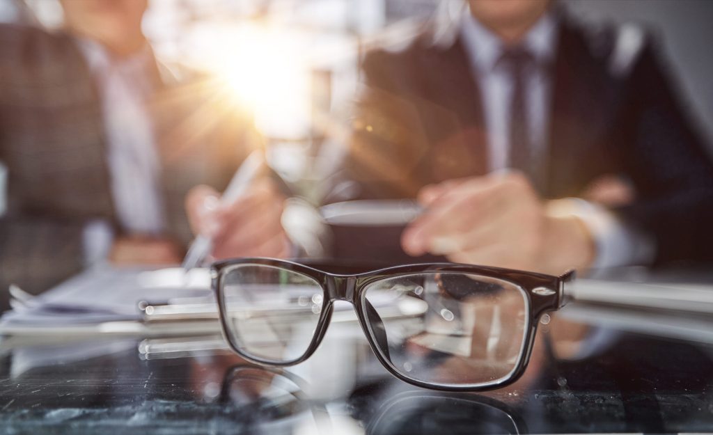 Close-up shot of business documents lying on meeting table, blurred silhouettes of male employees seen on background